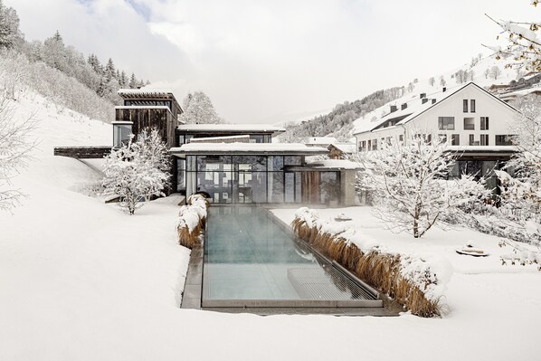 A modern building with a glass facade, surrounded by snow-covered trees and a clear sky.