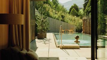 A modern interior with a pool, outdoor seating, and a view of a natural landscape.