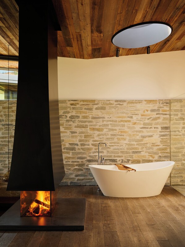 A modern bathroom with a freestanding bathtub, a stone wall, and a wood-burning stove. - Wiesergut (Saalbach-Hinterglemm)