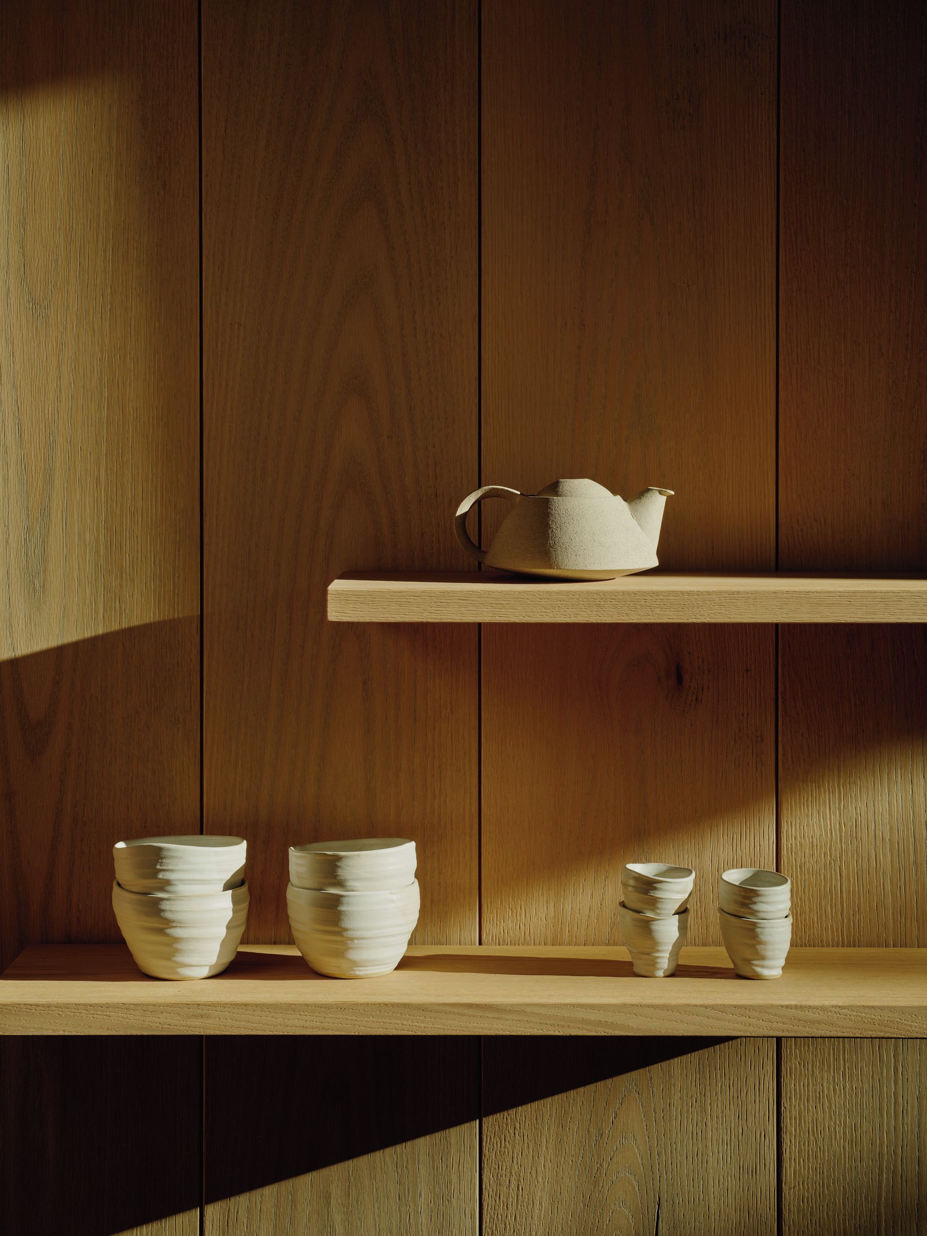 A wooden interior with two shelves, one holding a teapot and the other stacked bowls.