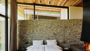 Un dormitorio moderno con pared de piedra, cama de madera y chimenea.