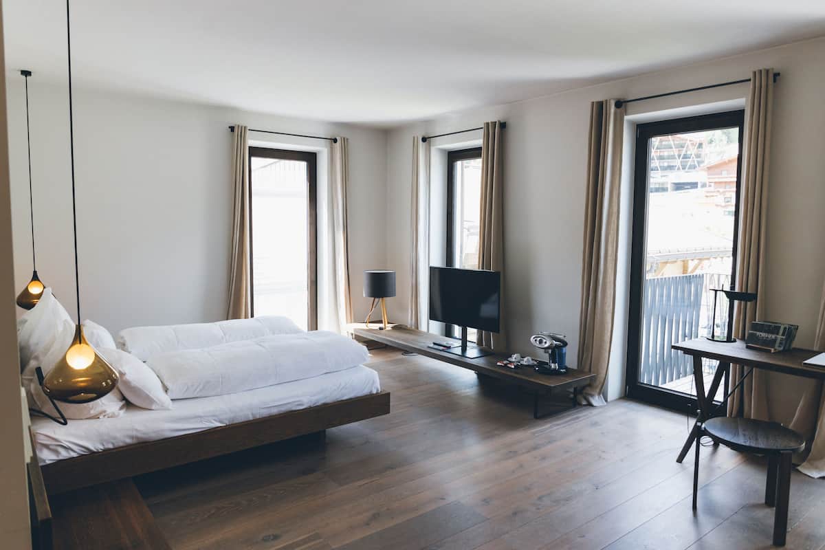 A modern hotel room with a bed, a desk, a TV, and large windows.
