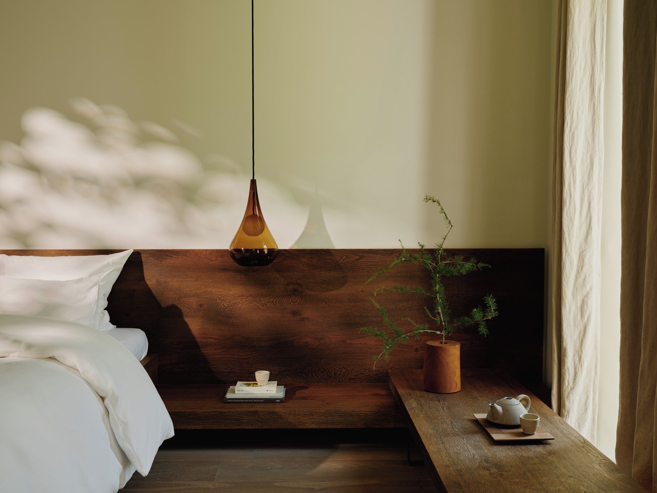 Un dormitorio acogedor con cabecera de madera, una mesita de noche con una planta y una tetera, y una lámpara colgante.