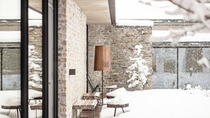 Un espacio de estar moderno al aire libre con paredes de piedra y bancos de madera, cubierto de nieve.