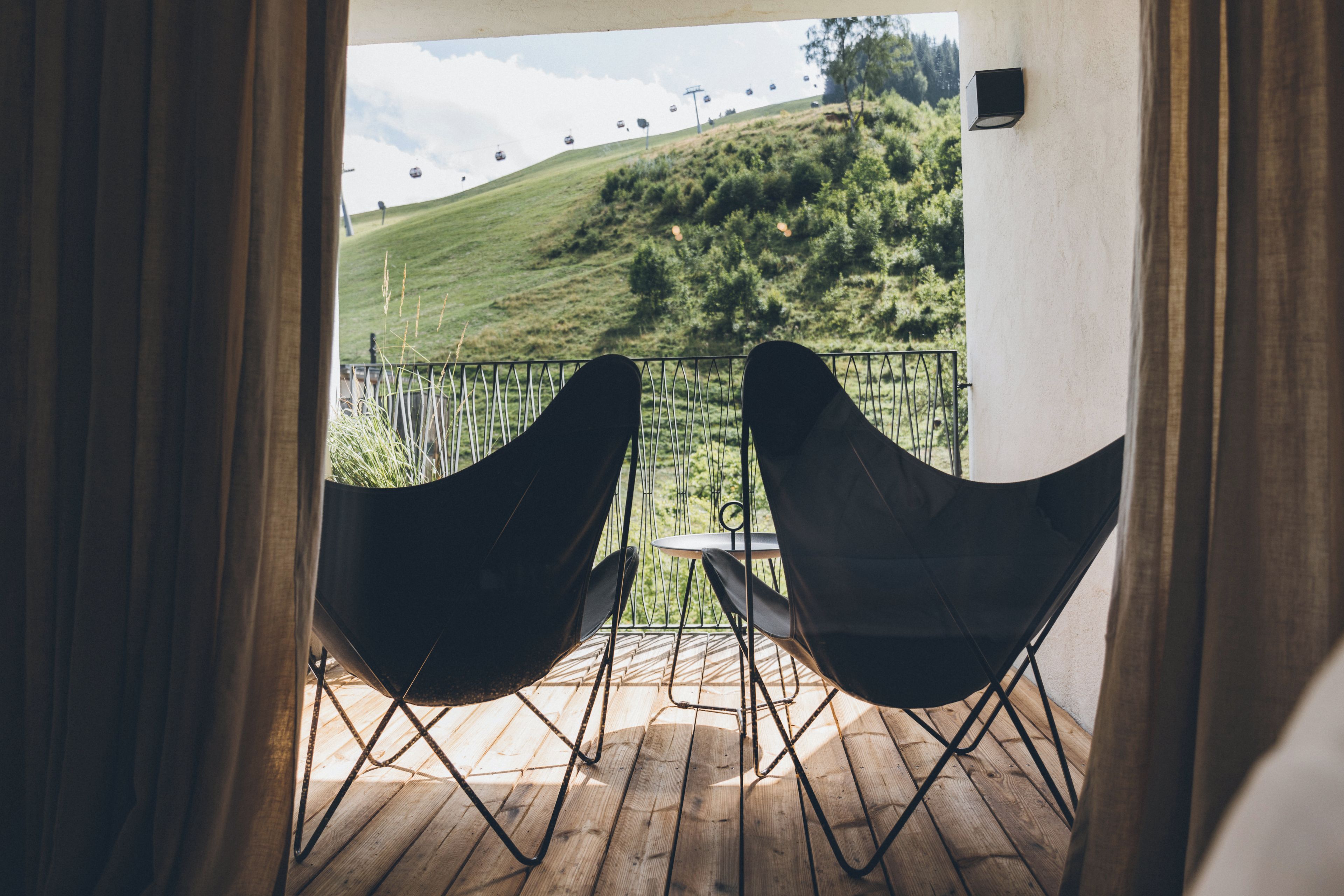 A balcony with two black chairs and a table, overlooking a grassy hill with a ski lift in the distance.