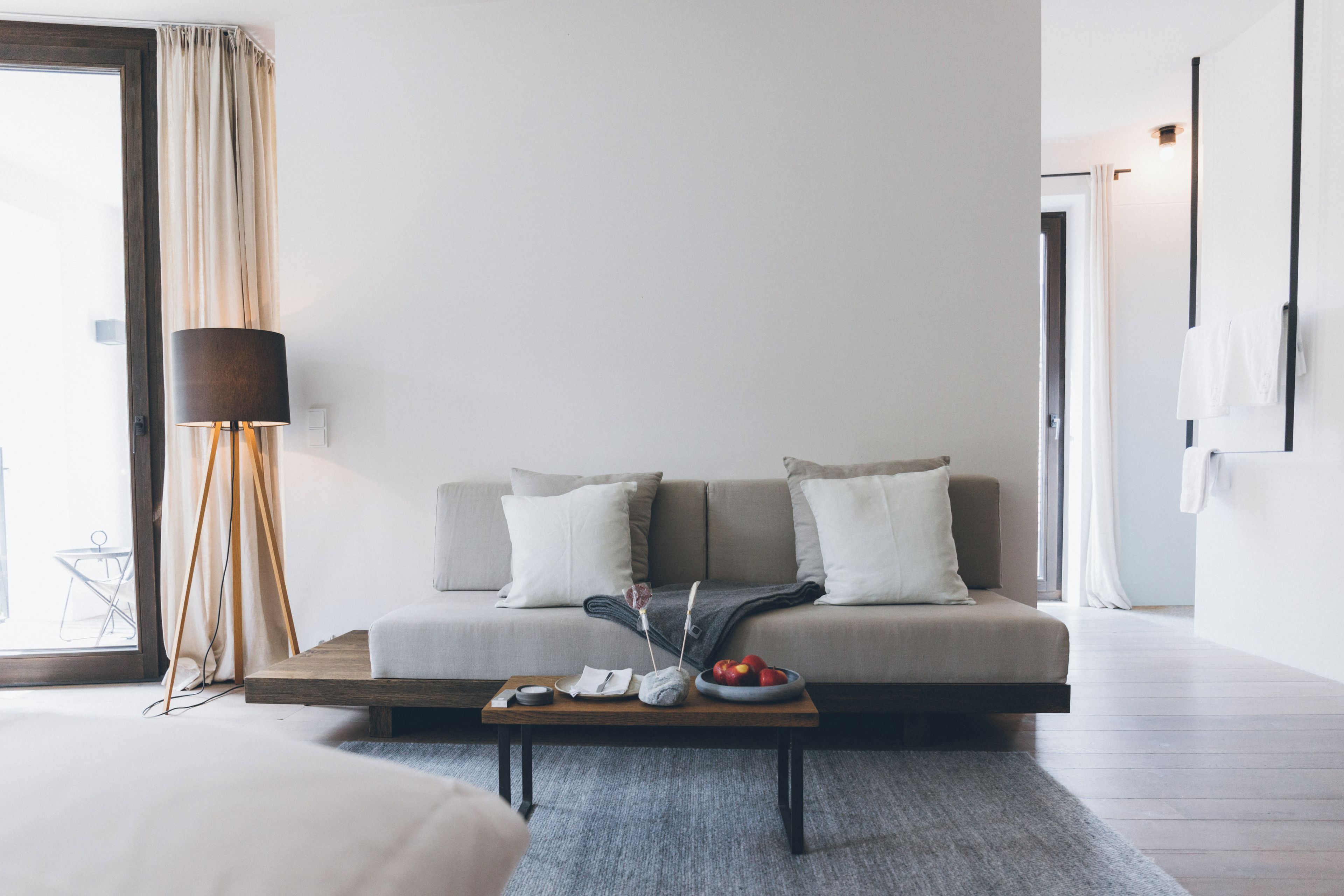 A modern living room with a sofa, a coffee table with fruits, a lamp, and a view of the outdoors.