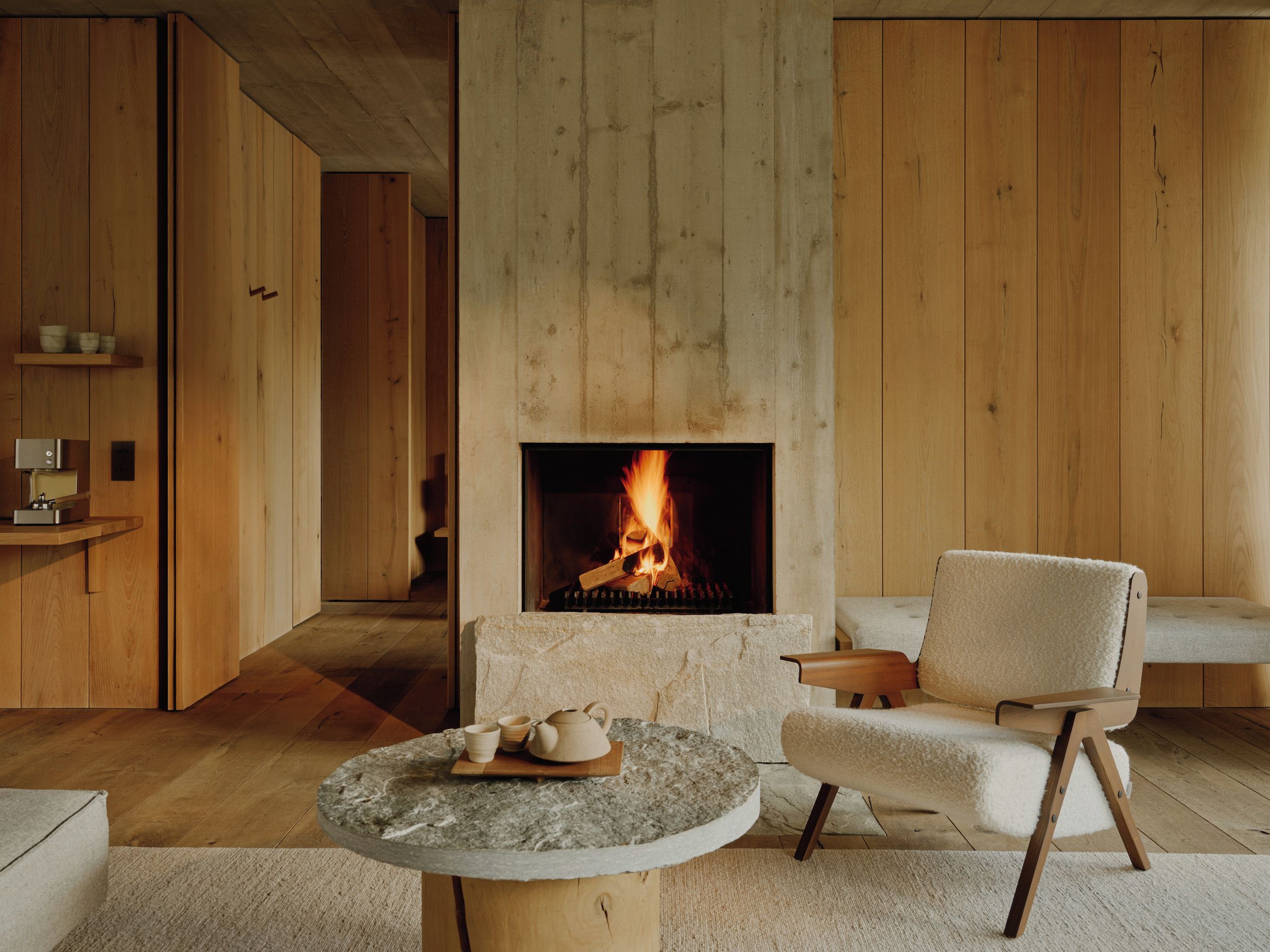 A modern living room with a fireplace, wooden paneling, a round stone table, and a comfortable chair.