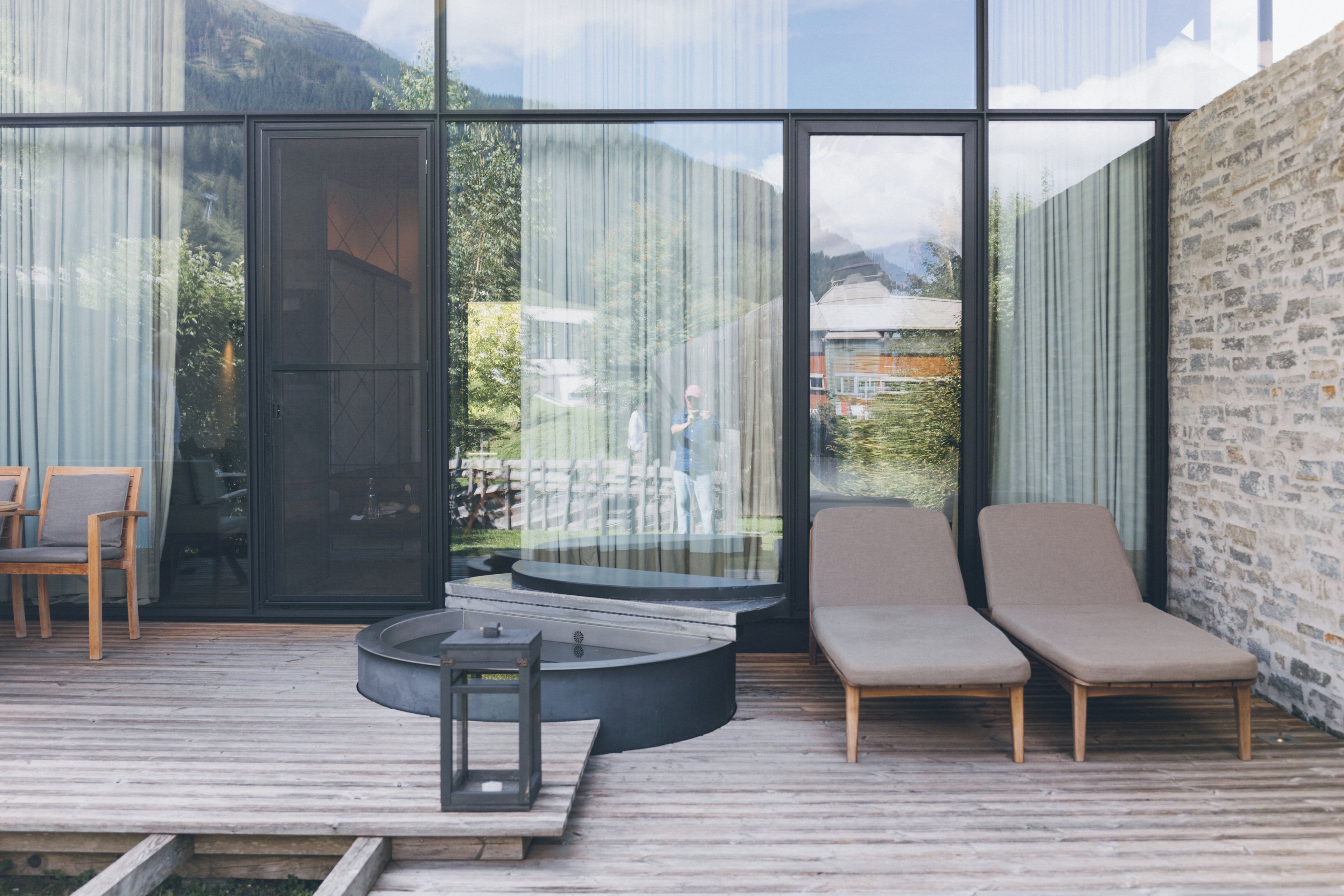 Un espacio de estar moderno al aire libre con terraza de madera, una mesa redonda y dos sillones de relax.