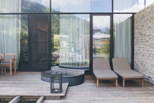 A modern outdoor seating area with a wooden deck, a round table, and two lounge chairs.