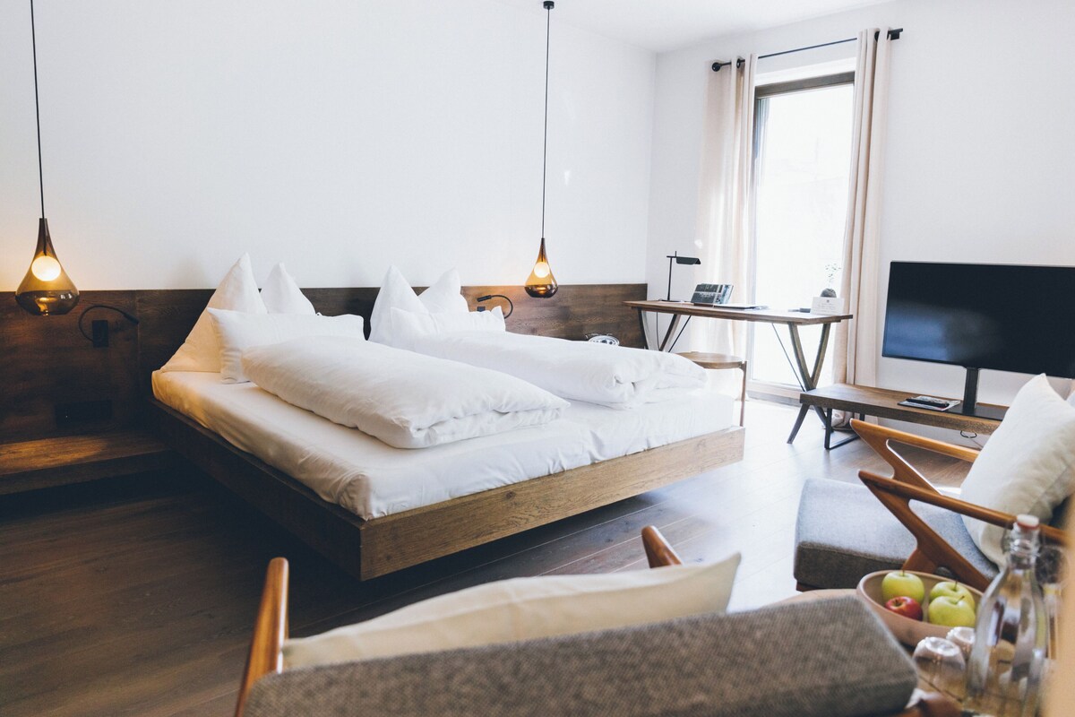A modern hotel room with a wooden bed, two pendant lights, a desk, and a television.