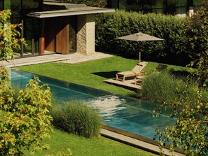 A swimming pool with a lounge chair and umbrella, surrounded by well-maintained grass and bushes. - Wiesergut (Saalbach-Hinterglemm)
