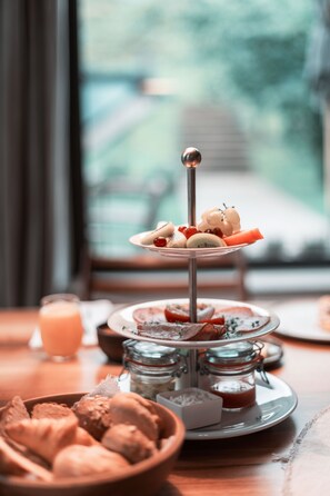 A three-tiered stand with food items, a glass jar, and a bowl of bread on a table. - Wiesergut (Saalbach-Hinterglemm)