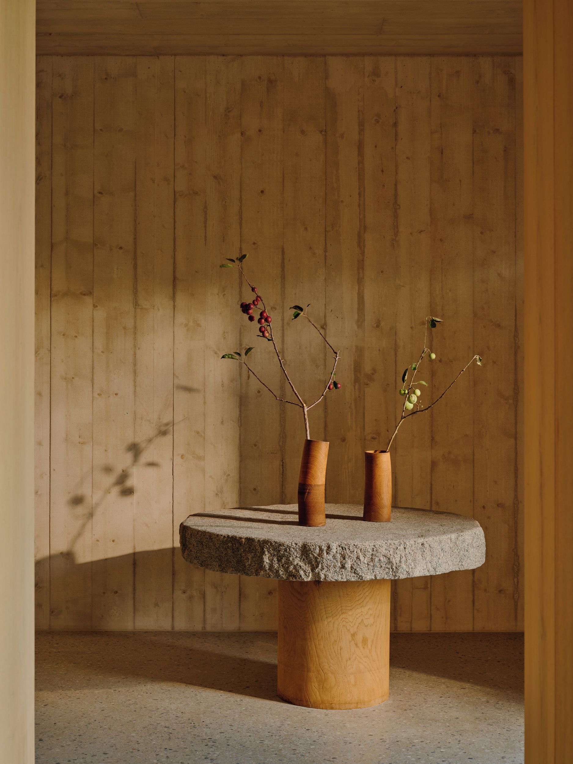 A round stone table with two wooden vases against a wooden wall.