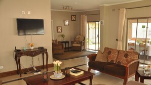 A living room with a sofa, coffee table, and a flat-screen TV mounted on the wall. - Coghlan Villa Guest House (Harare)