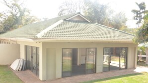 A single-story house with a tiled roof, large sliding glass doors, and a small patio area. - Coghlan Villa Guest House (Harare)