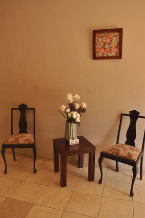 Una habitación con dos sillas, una mesita con un florero y un cuadro en la pared.