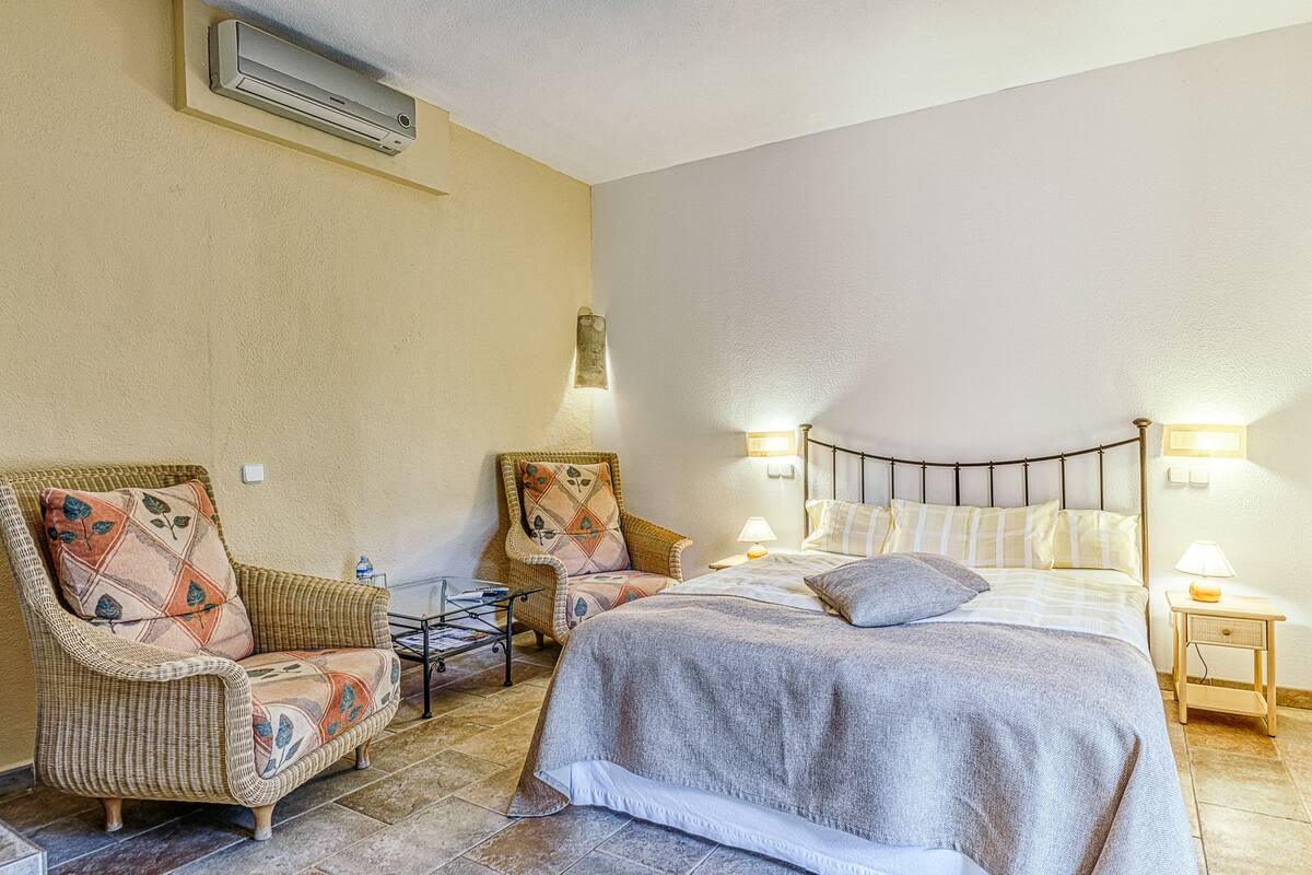 Une chambre à coucher comprenant un lit, deux fauteuils en osier, une petite table et deux lampes fixées au mur.
