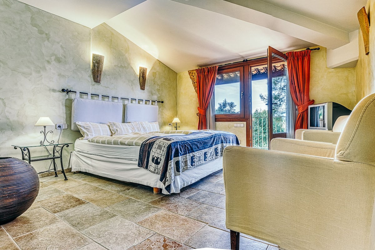 Une chambre à coucher avec un lit, des tables de chevet, une chaise, un téléviseur et une fenêtre avec des rideaux.