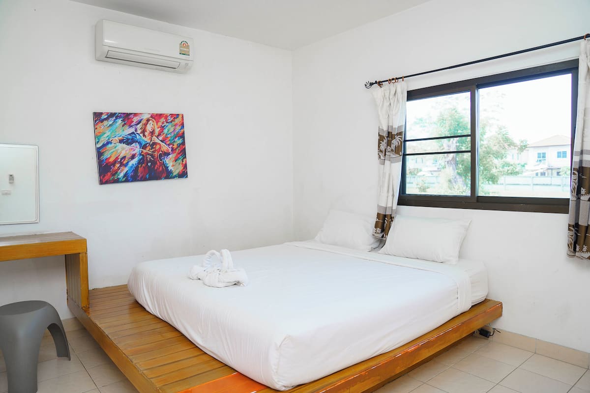 A bedroom with a bed, a desk, a chair, a window with curtains, and a painting on the wall.