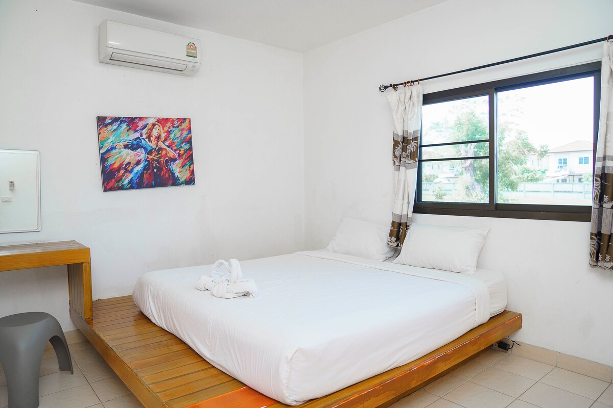 A bedroom with a bed, a desk, a chair, a window with curtains, and a painting on the wall.