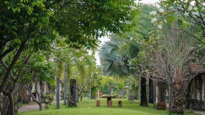 Ein gepflegter Garten mit verschiedenen Bäumen, einem zentralen Steinpflanzgefäß und einem Weg, der durch das Grün führt.