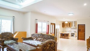 Ein geräumiges Wohnzimmer mit einer Sofagarnitur, einem Couchtisch mit Glasplatte und einem Essbereich mit Holzsesseln und einem Tisch.
