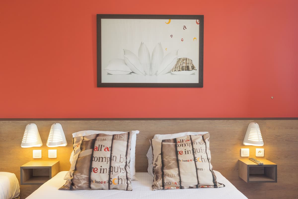 Een hotelkamer met een bed, twee bedlampjes, een kunstwerk boven het bed en een nachtkastje met een lamp.
