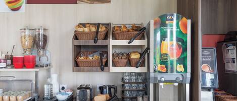 A hotel breakfast area with a coffee machine, bread baskets, and a fruit display.