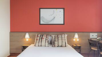 Habitación de hotel con cama, dos mesitas de noche, un escritorio con silla y una obra de arte abstracta enmarcada en la pared.