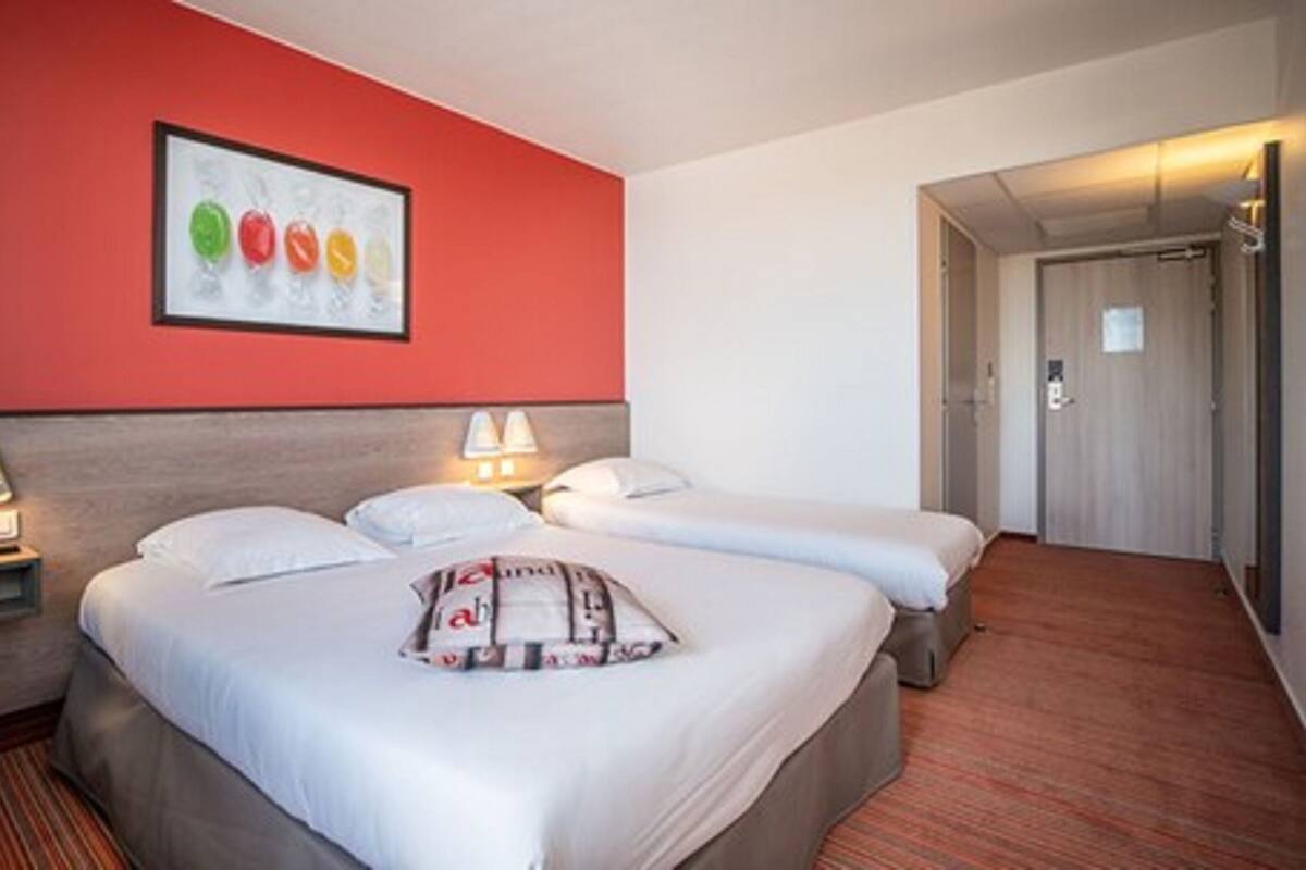 Een hotelkamer met twee bedden, een rode accentmuur en een lijst met kleurrijke objecten.