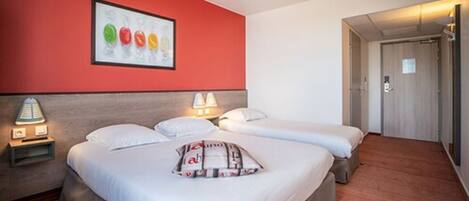 A hotel room with two beds, a red accent wall, and a framed picture of colorful objects.