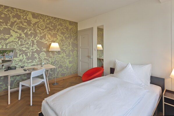 A hotel room with a bed, a desk with a chair, a red chair, and two lamps. - Boutique-Hotel Auberge Langenthal (Langenthal)
