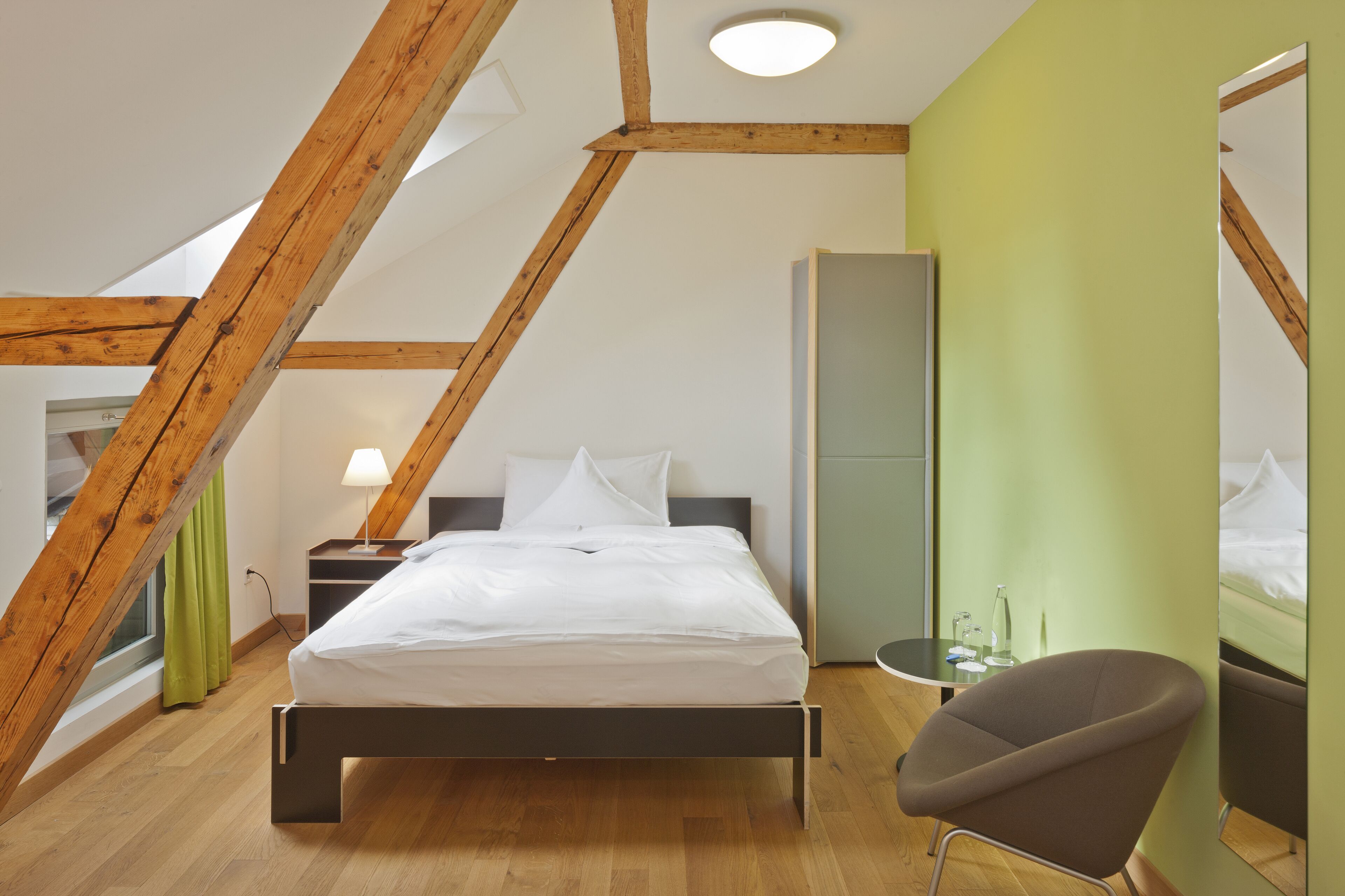 A modern bedroom with a sloped ceiling, a bed, a nightstand, a chair, and a tall cabinet.
