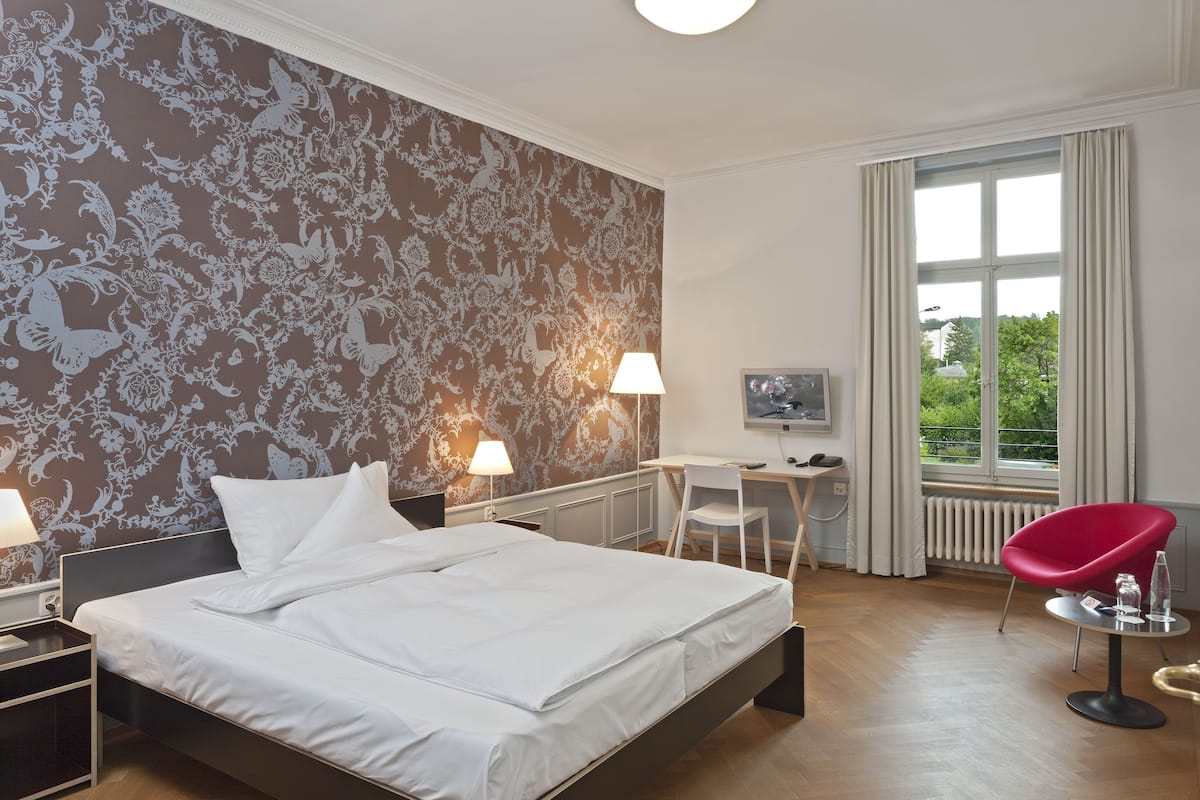 Une chambre d’hôtel avec un grand lit, un bureau, une chaise et une fenêtre avec des rideaux.