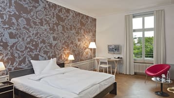 A hotel room with a large bed, a desk, a chair, and a window with curtains.