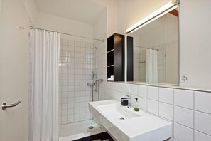 Un baño moderno con un lavamanos blanco, un espejo y una zona de ducha.