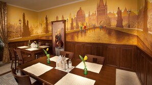 A dining area with a mural of a cityscape, wooden tables, chairs, and a vase with a flower. - Anyday Apartments (Prague)