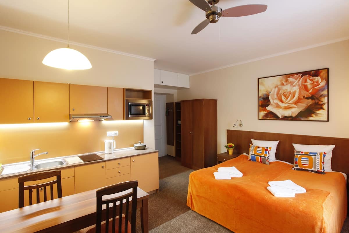 A hotel room with a bed, a desk, a chair, a microwave, a sink, and a ceiling fan.