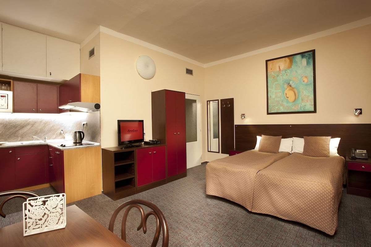 A hotel room with a bed, a desk with a chair, a television, a wardrobe, and a painting on the wall.