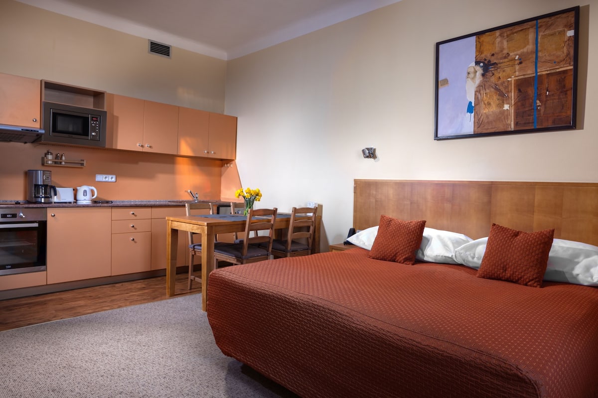 A hotel room with a bed, a desk, a chair, a microwave, a coffee maker, and a painting on the wall.