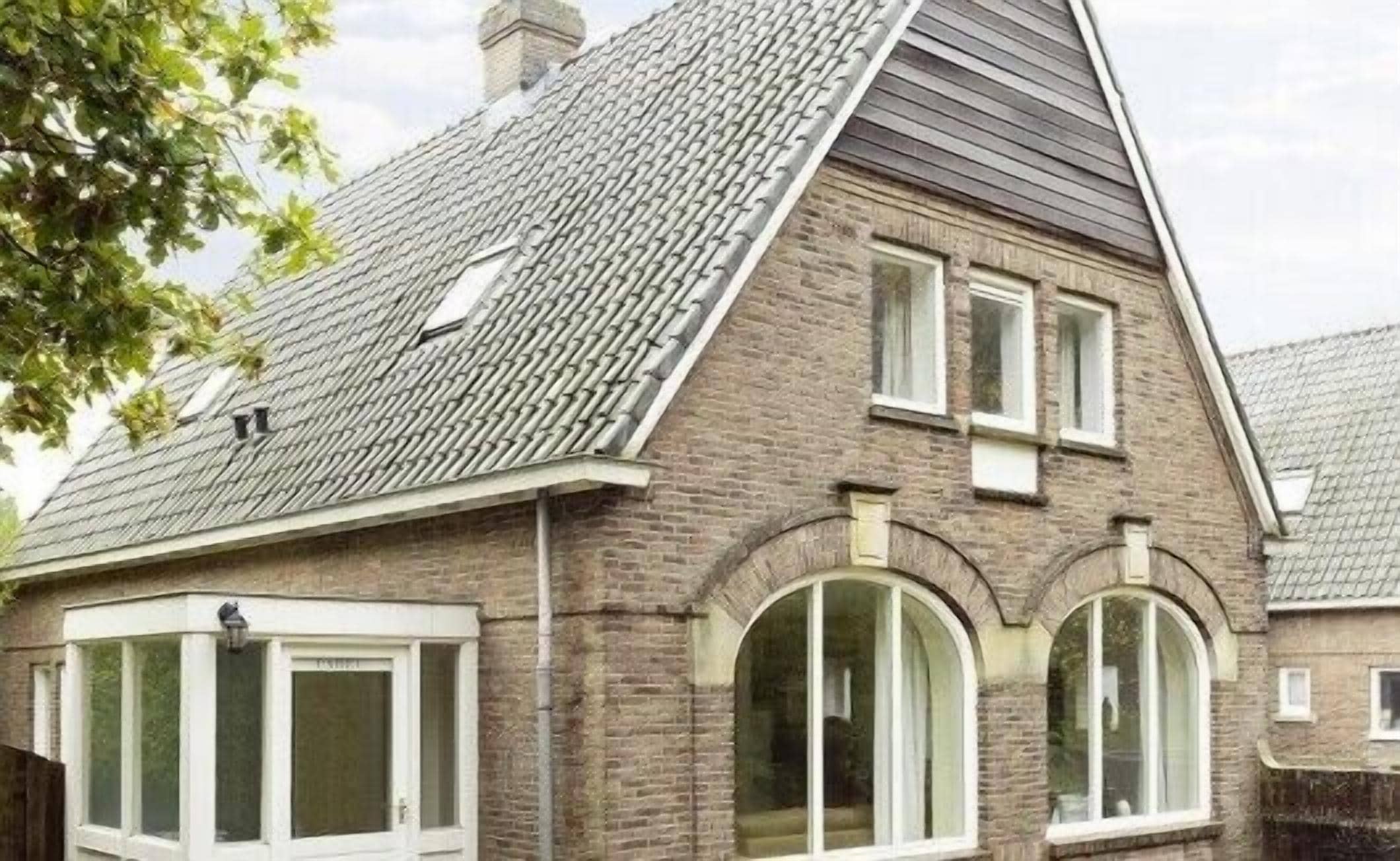 A two-story house with a sloped roof, brick exterior, and large arched windows.