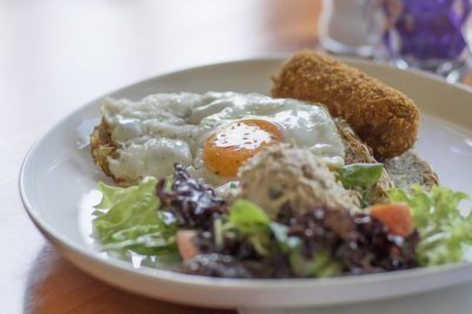 Een bord met een gebakken ei, een stukje paneermeelkip en een salade.