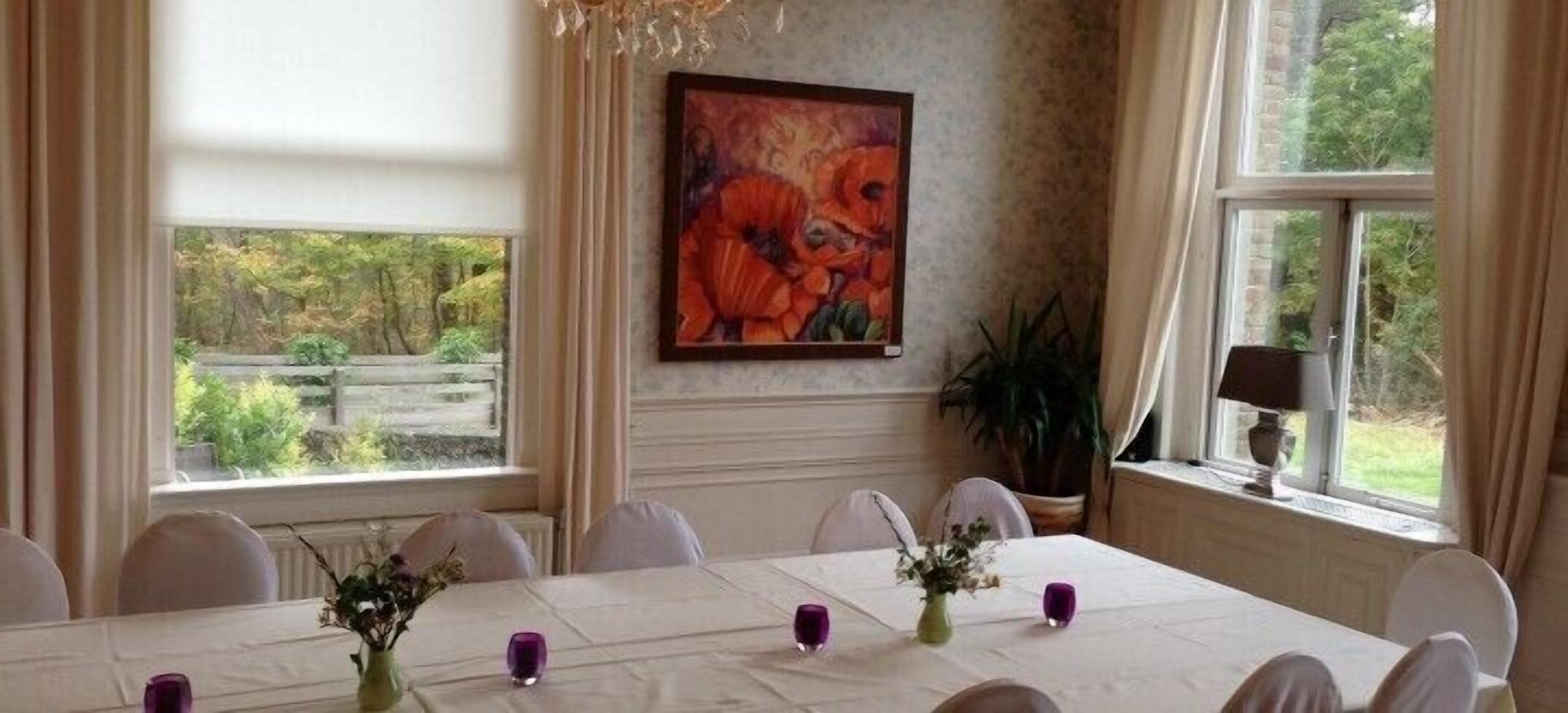 Ein Esszimmer mit einem Tisch für sechs Personen, großen Fenstern und einem Gemälde an der Wand.