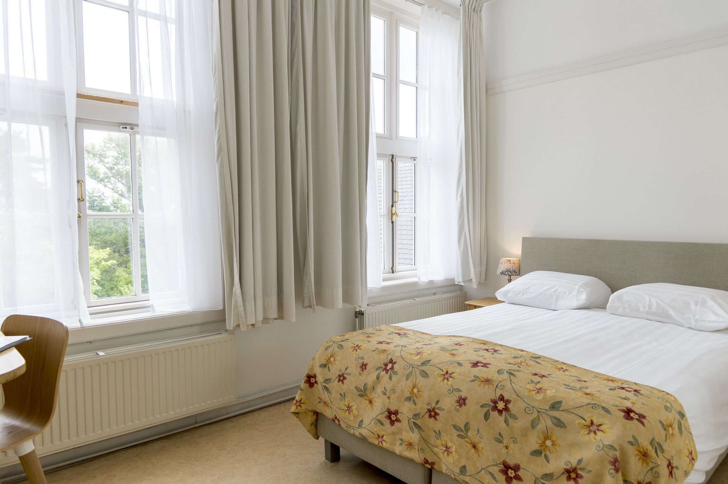 A bedroom with a bed, a chair, and a window with curtains.
