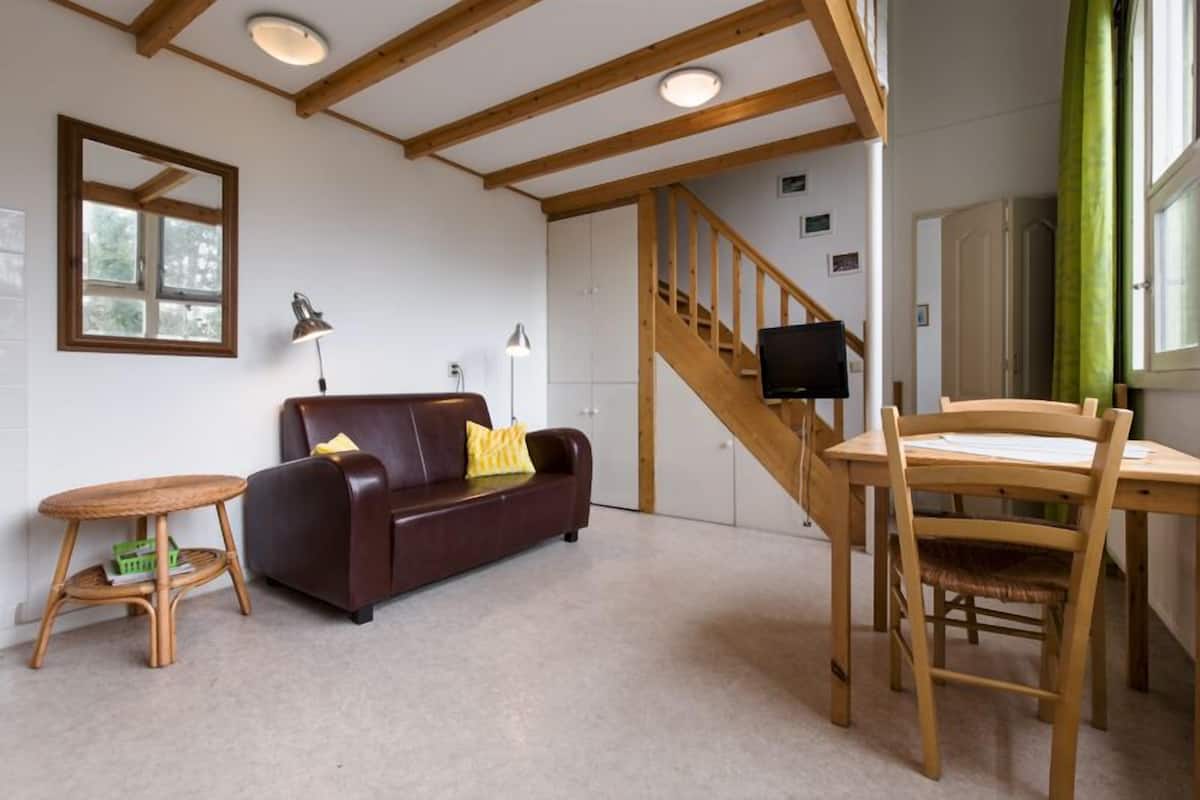A room with a wooden staircase, a brown leather sofa, a small round table, and a wooden dining table with chairs.
