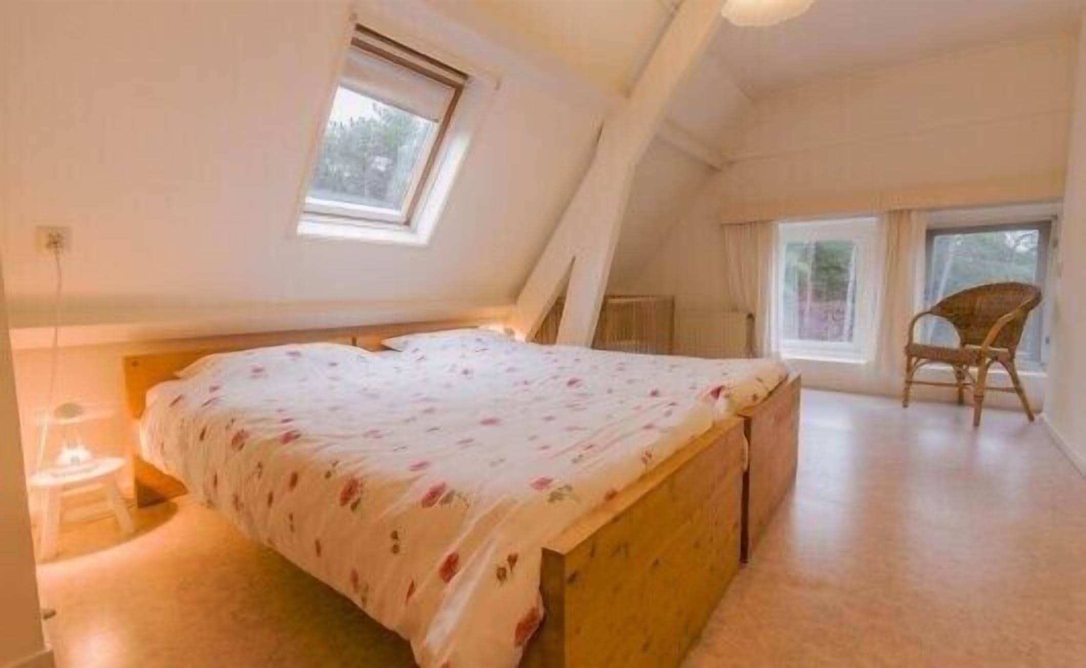 Un dormitorio con techo inclinado, una cama con colcha estampada, una silla y una ventana.