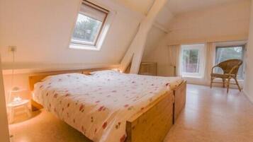 Un dormitorio con techo inclinado, una cama con colcha estampada, una silla y una ventana.