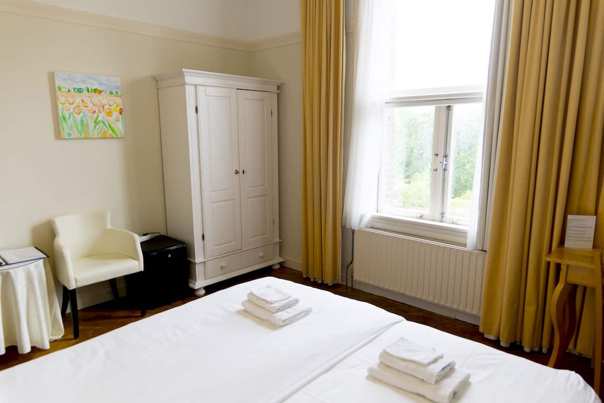 A hotel room with a bed, a chair, a wardrobe, and a window with curtains.
