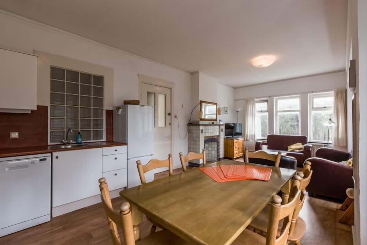 A compact kitchen with white cabinets, a wooden countertop, and a dining area with a wooden table and chairs.