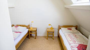 Cozy bedroom with two single beds, each with a wooden headboard and nightstand, featuring white linens with a red rose design.